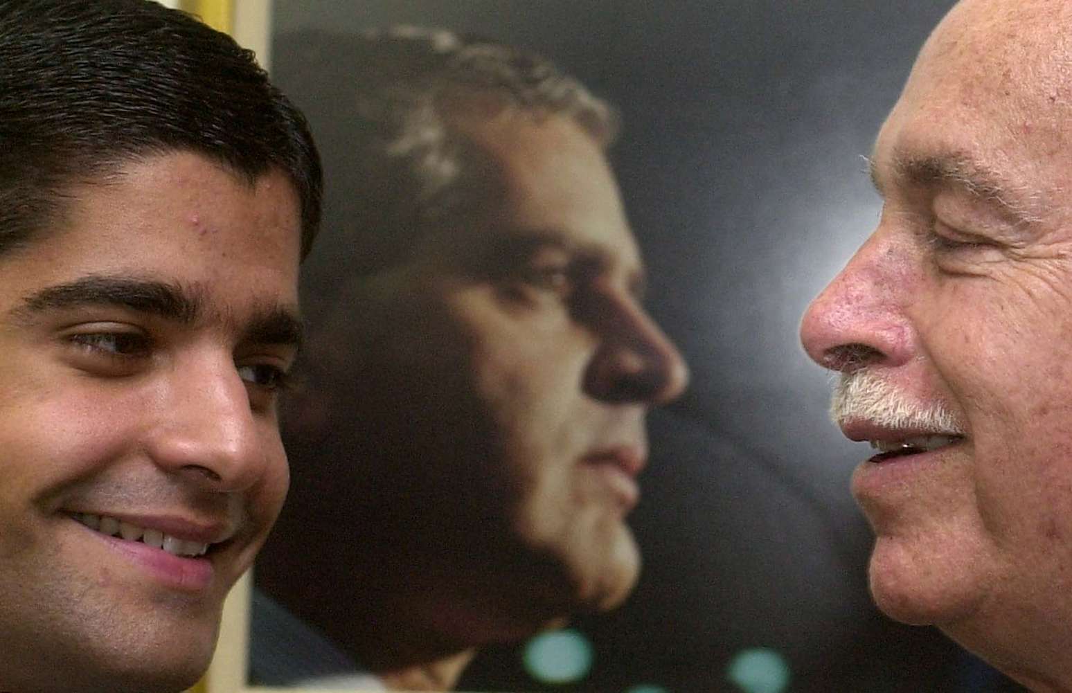 ACM sorri para seu neto ACM Neto no gabinete do também senador ACM Filho, em 2002. Ao fundo, foto de Antônio Carlos Magalhães Filho