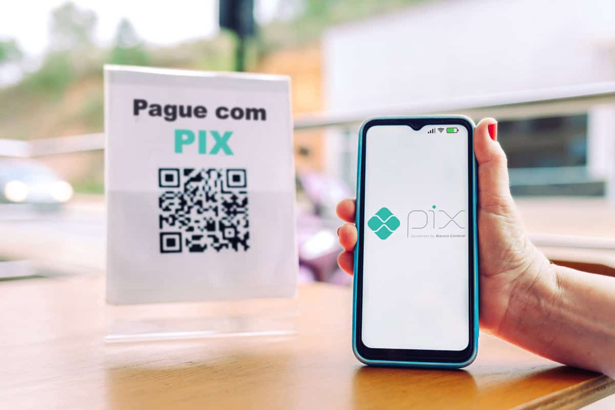 mão segurando um smartphone e escaneando um QR code em um suporte de acrílico para pagamento via PIX