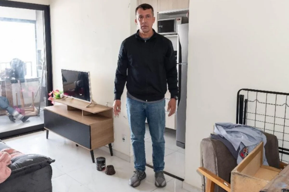 Homem branco, em pé, em sala de apartamento iluminado com a luz do dia - Metrópoles